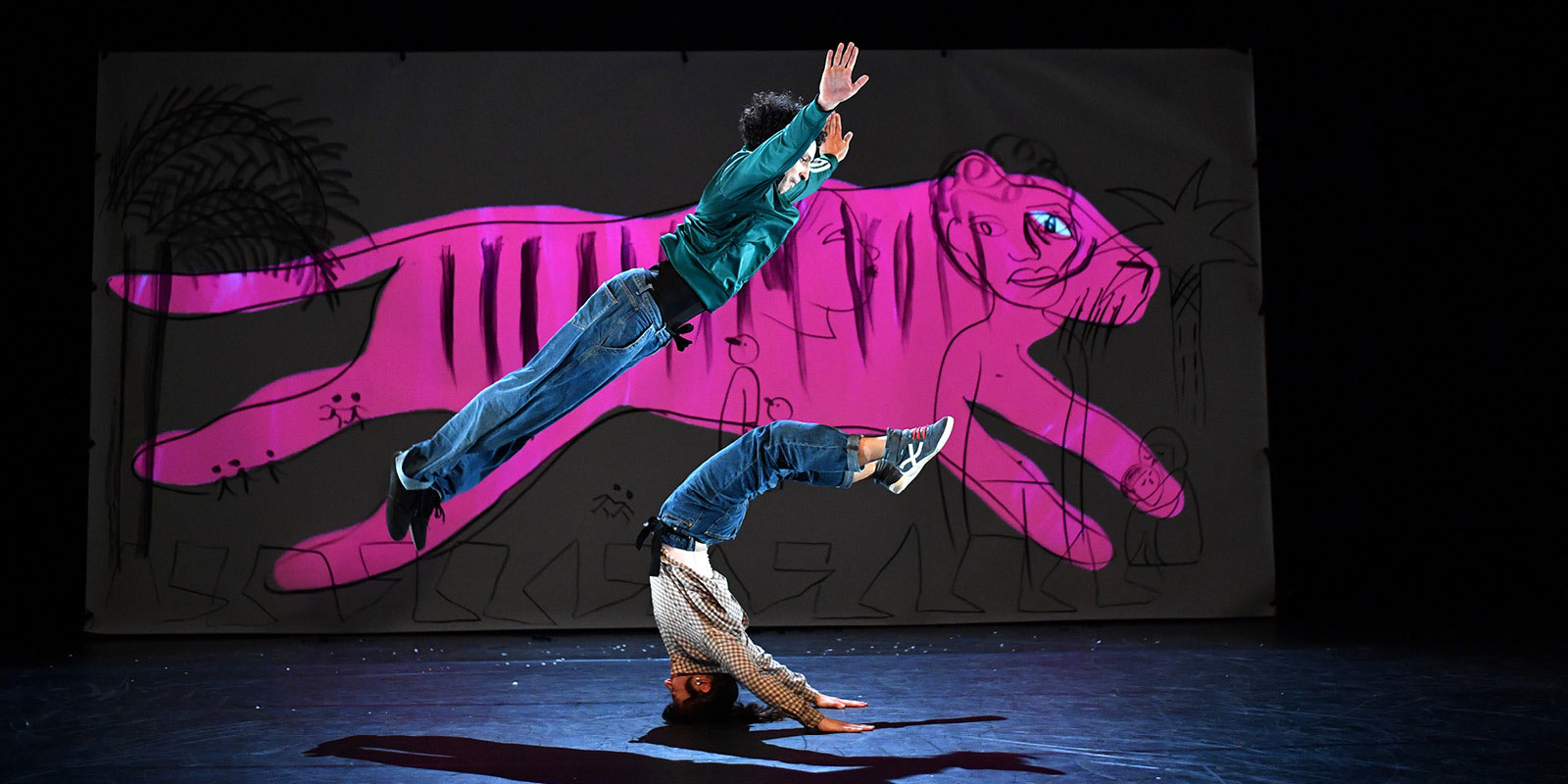 Photo issue du spectacle "Je suis tigre" avec deux acrobates en actions et un grand dessin projeté en fond de scène.