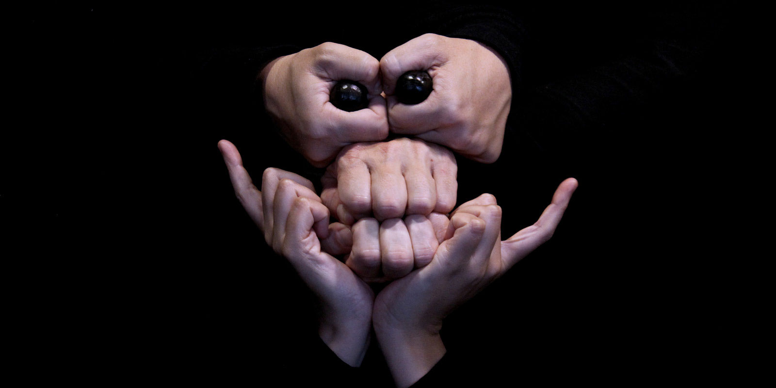 Photo d'un visage formé à partir de six mains. Des billes noires forment les yeux.